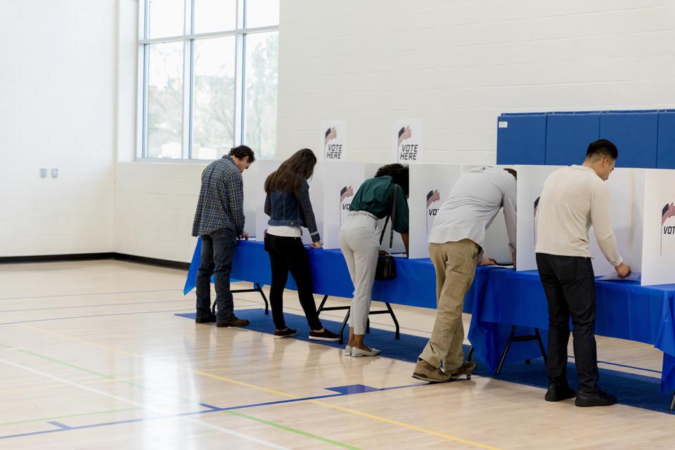 People stand at voting booths along the gym wall