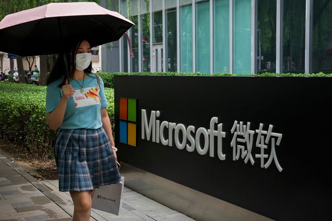 A woman wearing a face mask to help curb the spread of the coronavirus walks by the Microsoft office building in Beijing, Tuesday, July 20, 2021.
