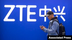 FILE - A man looks at his smartphone as he stands near a display for Chinese technology company ZTE at the PT Expo in Beijing on Oct. 31, 2019.