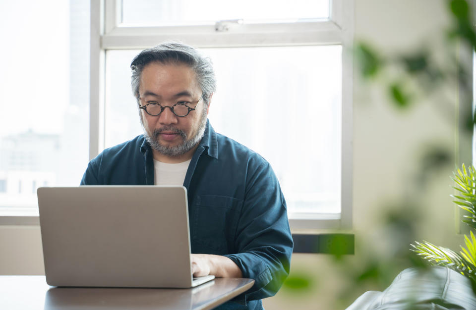 Middle-aged Asian man using laptop work from home.