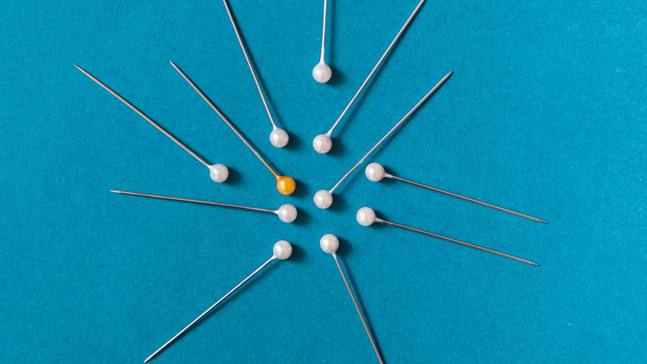 Pinning concept; overhead view of yellow and white push pins on a blue background